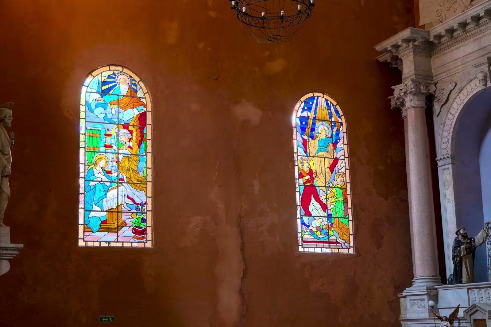 Sunlight passing through two stained-glass windows inside a warm terracotta church